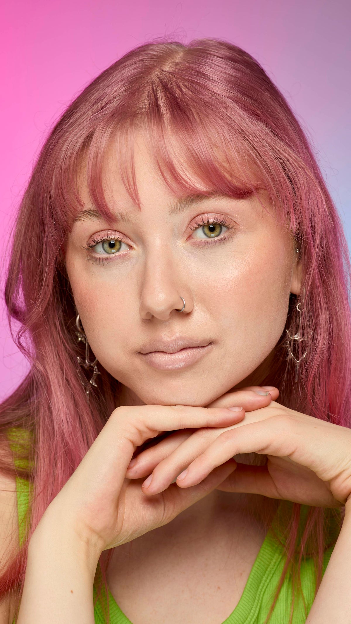 The image shows a fair-skinned model on a pink and blue gradient background. They have pink hair and subtle, peach-nude shimmering lips from using the Peach parfait lip cream.